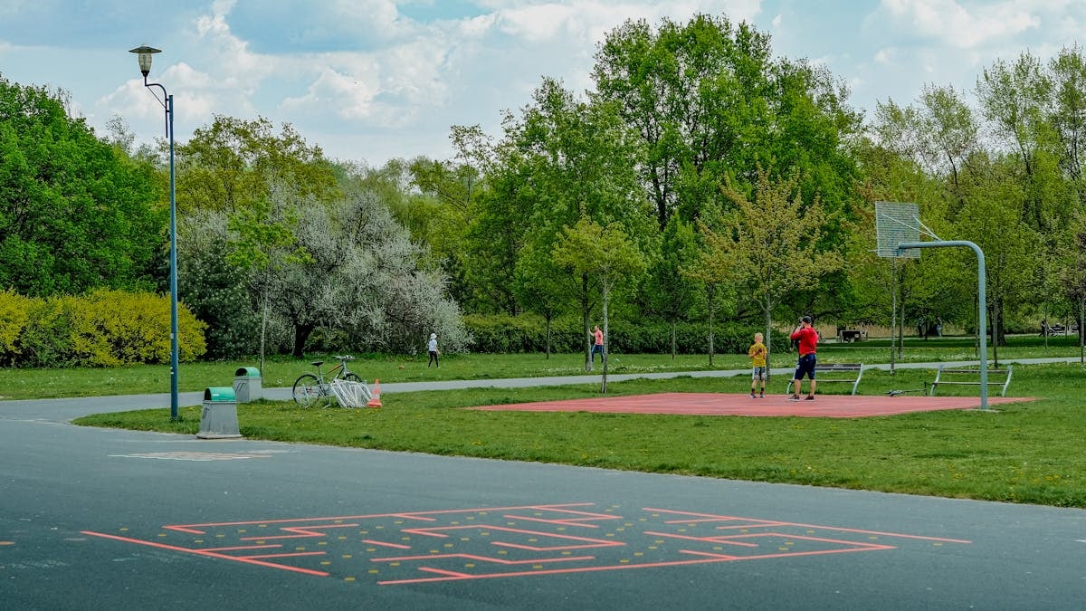 A father and child enjoy playing basketball on an outdoor court in a green, tranquil park setting.